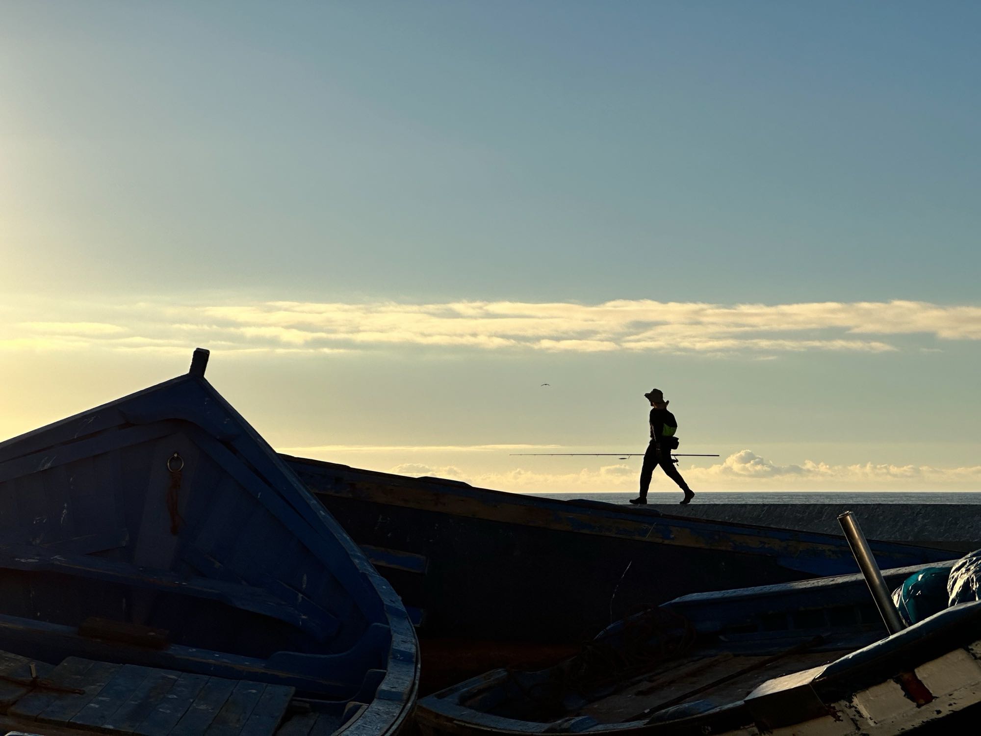 A silhouetted person walking past fishing boats at sunset