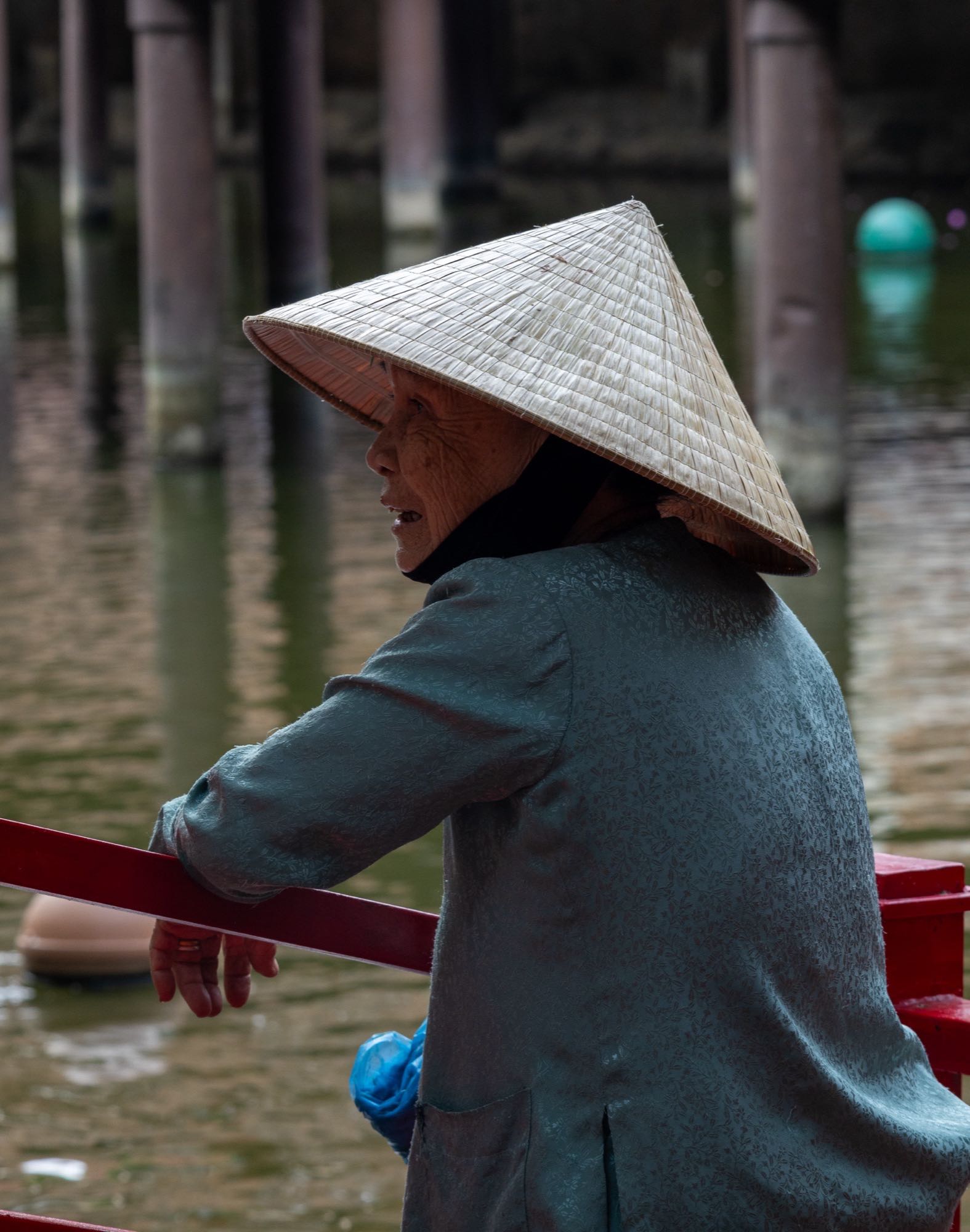 A person in a conical hat standing by water inside a city temple complex